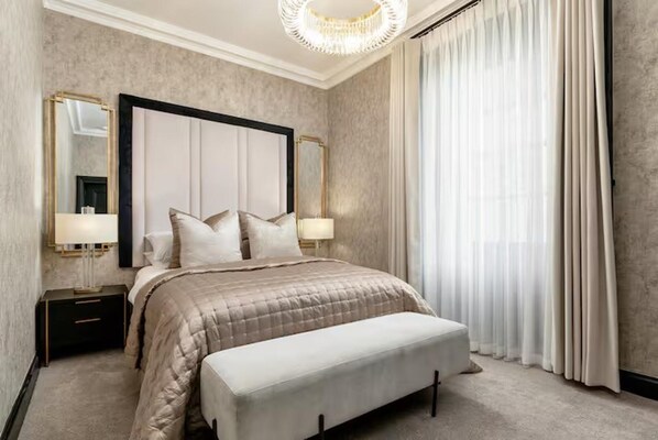 A bedroom with a large bed, two bedside tables, a bench, a chandelier, and a large mirror. - Near Transport - Hot tub - Fireplace - Sleeps 2 (Edinburgh)