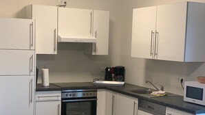 Moderni keittiö, jossa on valkoiset kaapit, sisäänrakennettu uuni, kahvinkeitin ja mikroaaltouuni.