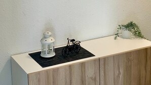 Kehyksiin asetettu maisemamaalaus, jossa on esitetty maalaistie ja peltoja, valkoinen lyhty, polkupyörä ja pieni ruukkukasvi puisen kaapin päällä.