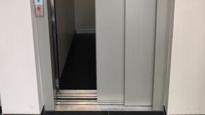 Een lift met een metalen interieur, een handgreep en een bedieningspaneel met een rode knop.