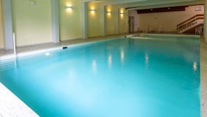An indoor swimming pool with a clear blue water surface, surrounded by walls with light fixtures and a staircase leading to an upper level. - Arosa - alles komplett by Interhome (Arosa)
