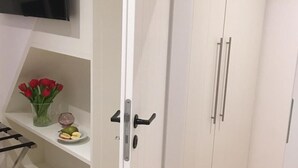 Quarto com armário branco, prateleira com tulipas vermelhas e televisão de tela plana na parede.