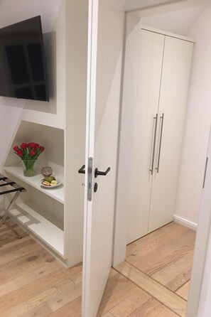 A room with a white wardrobe, a shelf with red tulips, and a flat-screen TV mounted on the wall. - DünenHuuske "InselFreid" mit Sauna auf Spiekeroog by Interhome (Spiekeroog (Ort))