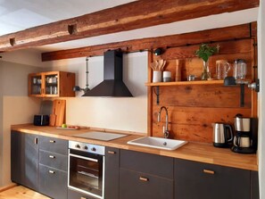 Une cuisine moderne avec des poutres en bois, un four encastré, un évier et divers ustensiles de cuisine rangés sur des étagères.