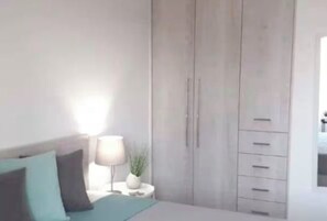 A bedroom with a bed, a nightstand with a lamp, and a wardrobe. - Renovated seaside apt for families with 1 kid : sea view, full kitchen, Wi-Fi (Kato Gouves)