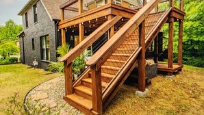 Une maison à deux étages avec une terrasse en bois et un escalier menant à un porche abrité.