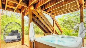Une terrasse en bois avec un jacuzzi, un fauteuil suspendu et un escalier menant à un niveau supérieur.