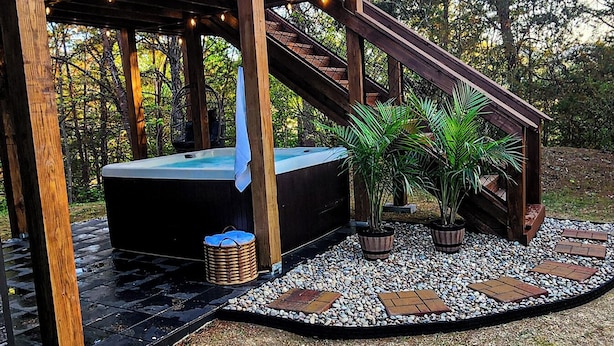 Une terrasse en bois avec un jacuzzi, des plantes en pot et un chemin de pierre.