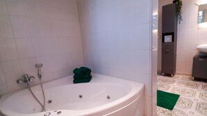 Une salle de bain avec une grande baignoire, une douche et des toilettes. Il y a une serviette verte sur le sol et une plante accrochée au mur.