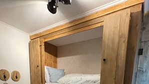 Ein Etagenbett mit einer Stehleiter, einem Holz-Kopfteil und einem kleinen Regal.