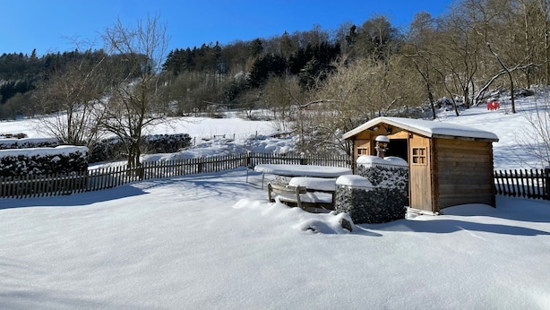 Eine Holzhütte mit schneebedecktem Dach, umgeben von einem Holzzaun und verschneitem Gelände.