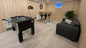 Ein Zimmer mit Tischfußballtisch, einer Couch und einer kleinen Bar mit Hockern.