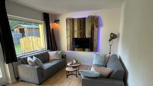 Ein modernes Wohnzimmer mit zwei grauen Sofas, einem kleinen runden Tisch und einem an einer Holzwand montierten Fernseher.