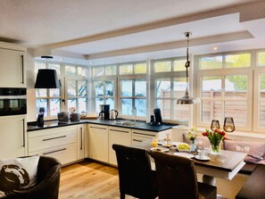 Una cocina moderna con ventanas amplias, un comedor con una mesa lista para el desayuno y un rincón de estar acogedor.