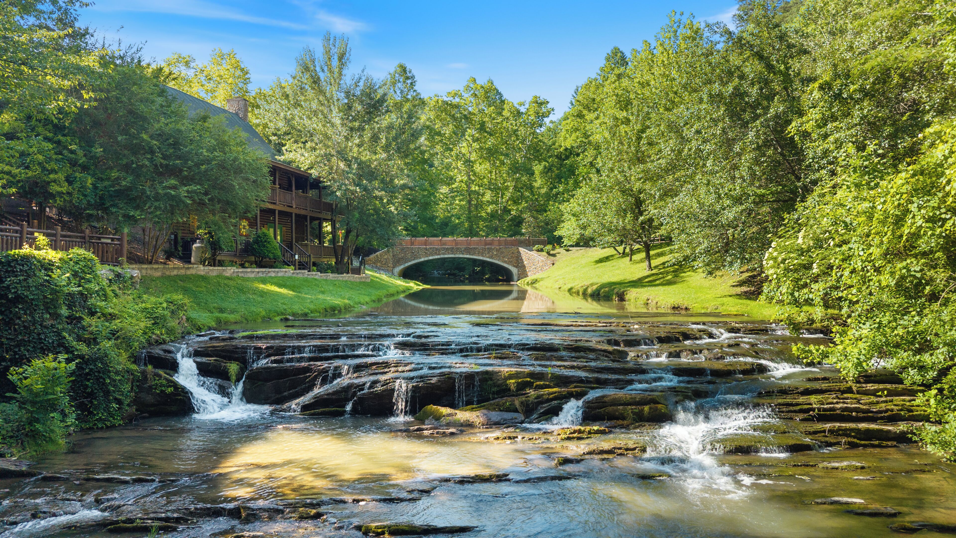 A natural water feature with a wooden bridge and a building with a porch.