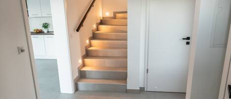 A modern interior with a staircase leading to a second floor, a wooden bench, and a white door.