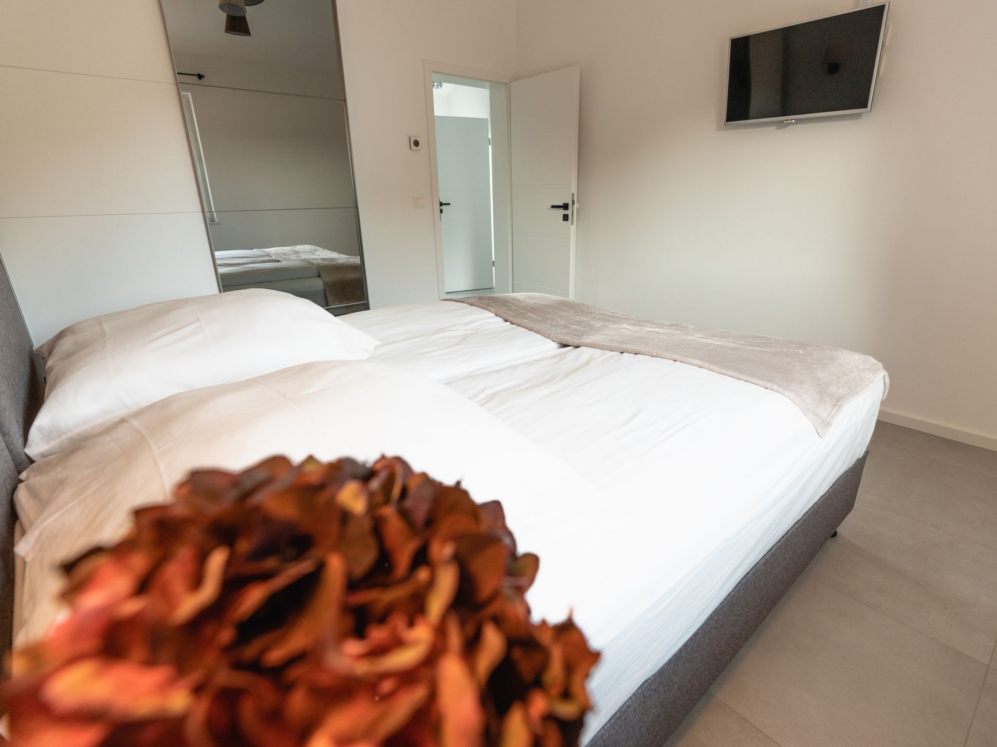 A modern hotel room with a large bed, a television mounted on the wall, and a door leading to a bathroom.