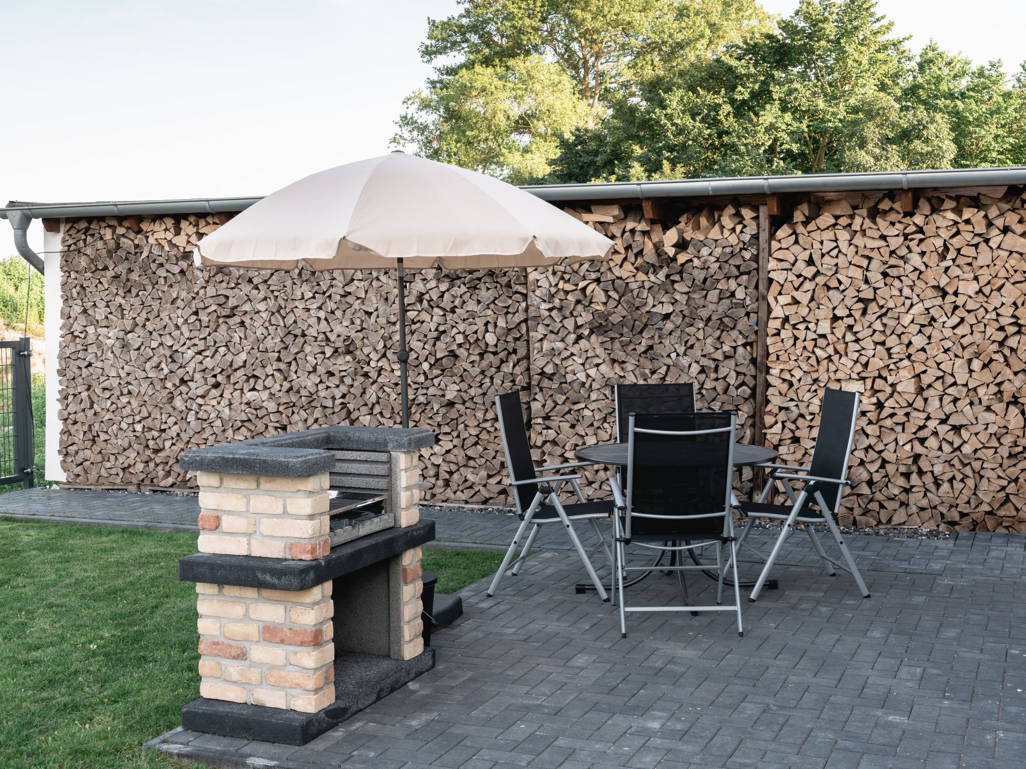 Une terrasse extérieure avec un barbecue en briques, deux chaises pliantes et une table.