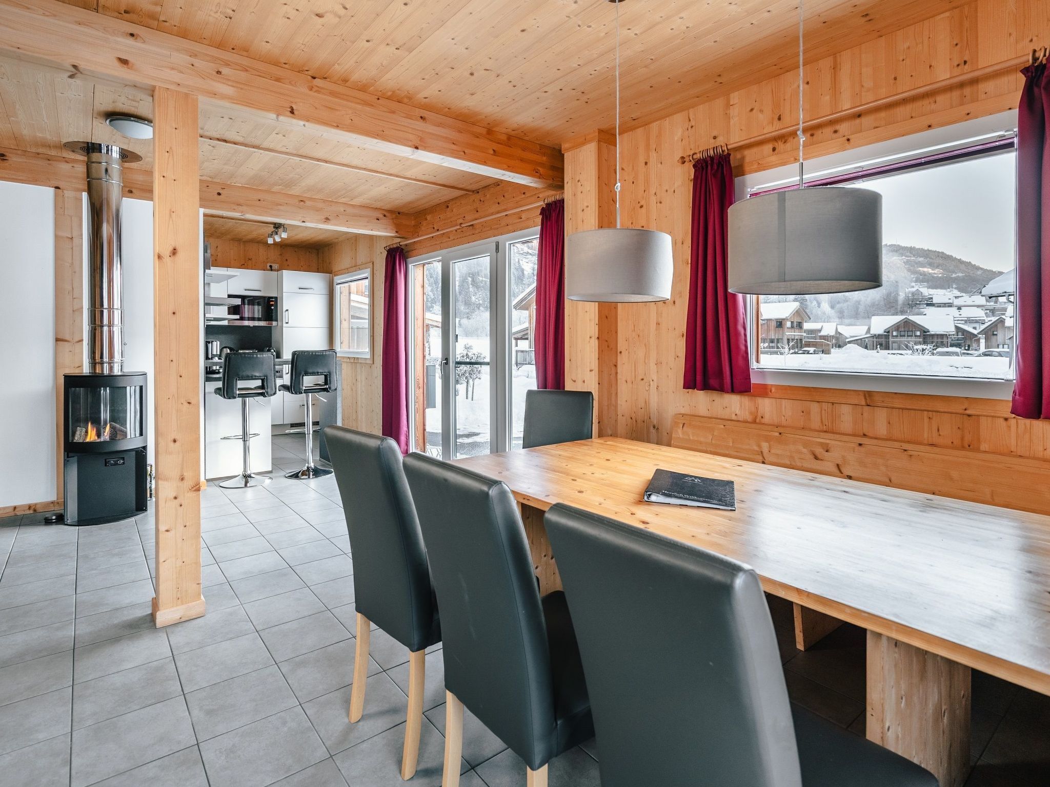 A modern interior with a wooden dining area, black chairs, a long table, and a kitchen in the background.