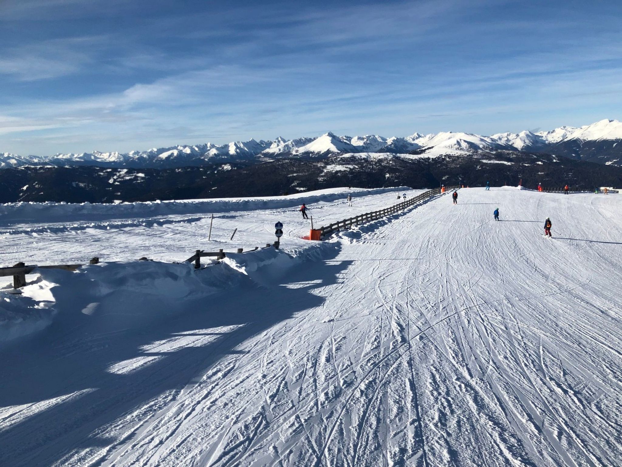 A snowy ski slope with a wooden fence and a clear sky.