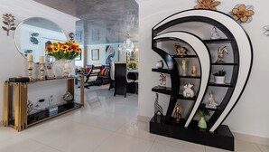 Ein modernes Wohnzimmer mit einem Glastisch, einem schwarz-goldenen Konsolentisch und einer schwarzen Regaleinheit mit Dekorationselementen.