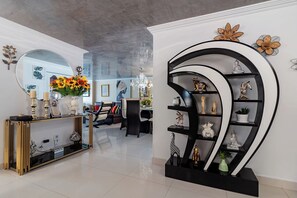 A modern living room with a glass coffee table, a black and gold console table, and a black shelving unit with decorative items. - 3-bedroom Luxury Apartment in Cartagena with AC on the Beach (Cartagena de Indias)