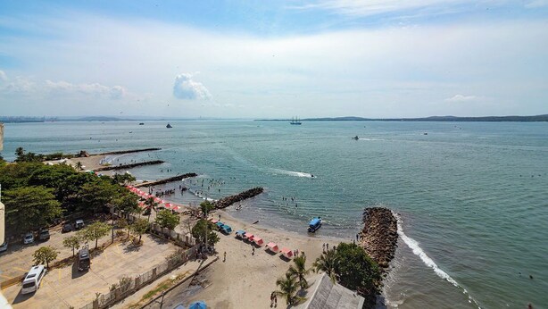 Blick auf die Küste mit Strand, einem Steg und einem Schiff in der Ferne.