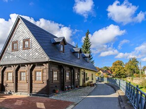Ein traditionelles Holzhaus mit einem steilen Dach, einem Kopfsteinpflasterweg und einem blauen Metallgeländer an der Seite.