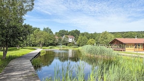 A wooden boardwalk leading to a pond with a pavilion and a house in the background.