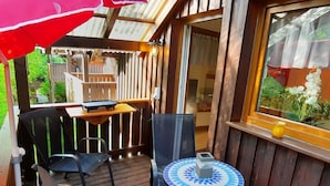 A wooden deck with a table and chairs, a small round table with a decorative tile top, and a red umbrella.