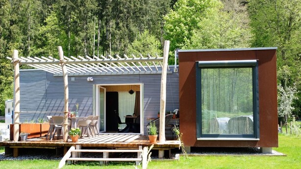 Un rifugio moderno con una veranda, posti a sedere all'aperto e un'ampia finestra.