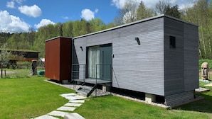 Una casa moderna con facciata grigia, un'ampia porta scorrevole in vetro e una piccola finestra.