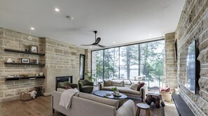 A spacious living room with a fireplace, large windows, and a stone wall. - 7 bed 7 bath cottage on Lake Joseph (Parry Sound)