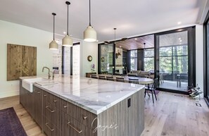 A modern kitchen with a marble island, pendant lighting, and a dining area with a view. - 7 bed 7 bath cottage on Lake Joseph (Parry Sound)