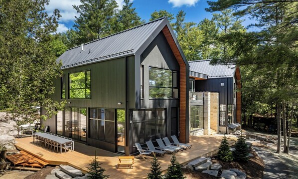 A modern cabin with a deck, large windows, and a stone foundation. - 7 bed 7 bath cottage on Lake Joseph (Parry Sound)