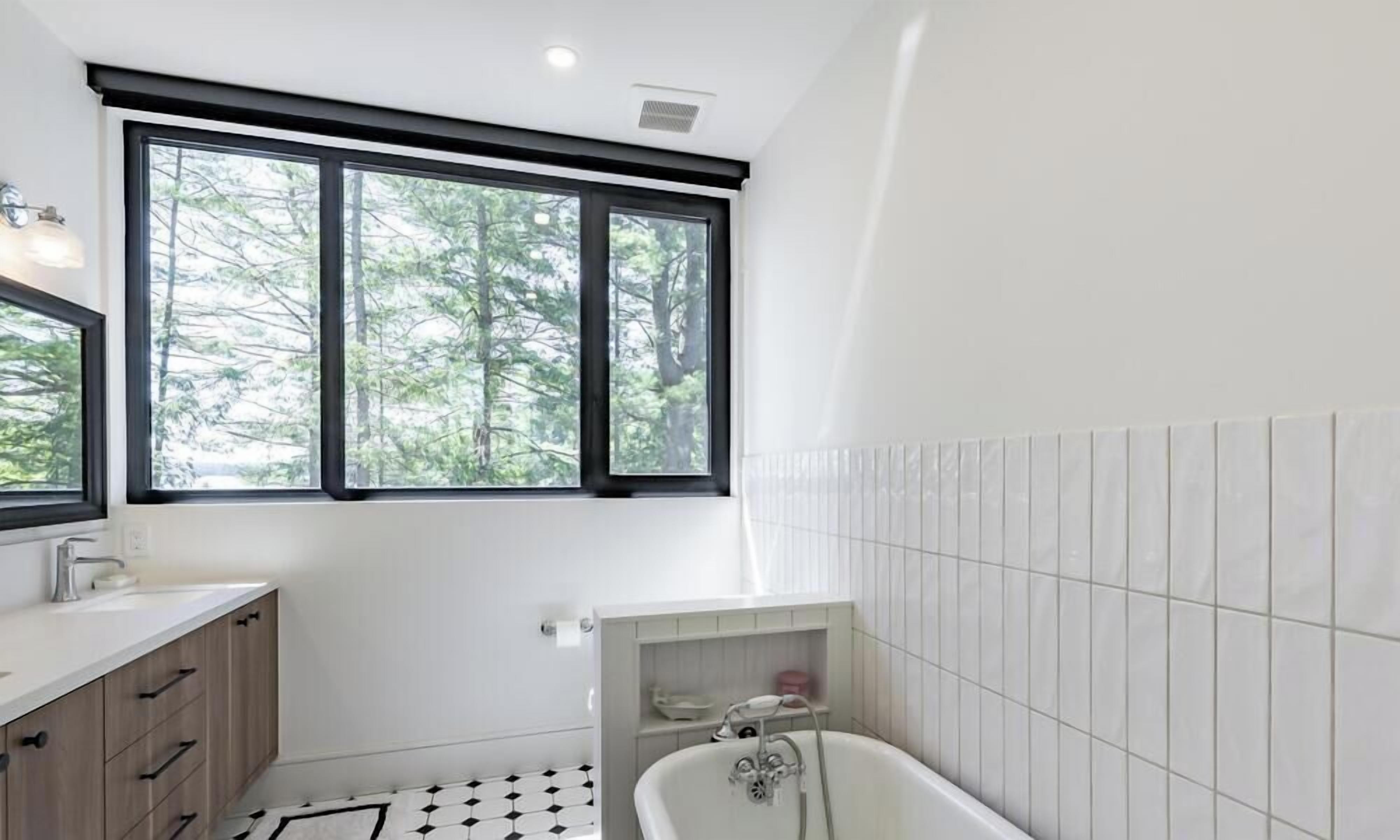 A modern bathroom with a bathtub, a window with a view of trees, and a tiled floor.