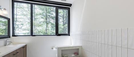 A modern bathroom with a bathtub, a window with a view of trees, and a tiled floor.