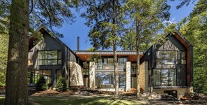 A modern cabin with large windows, a stone facade, and a fire pit in the yard. - 7 bed 7 bath cottage on Lake Joseph (Parry Sound)