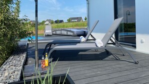Une terrasse avec deux chaises longues, une piscine et une bouteille de jus d’orange.