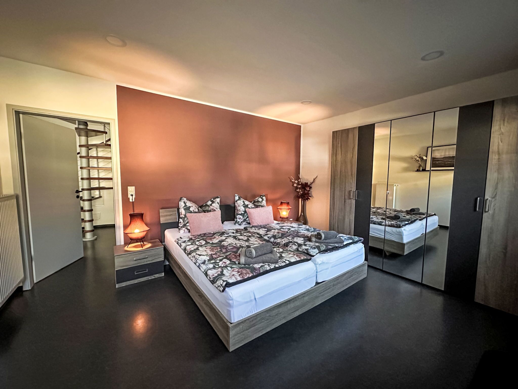 Ein modernes Schlafzimmer mit einem großen Bett, einem Kleiderschrank, einem Spiegel und einer Treppe.