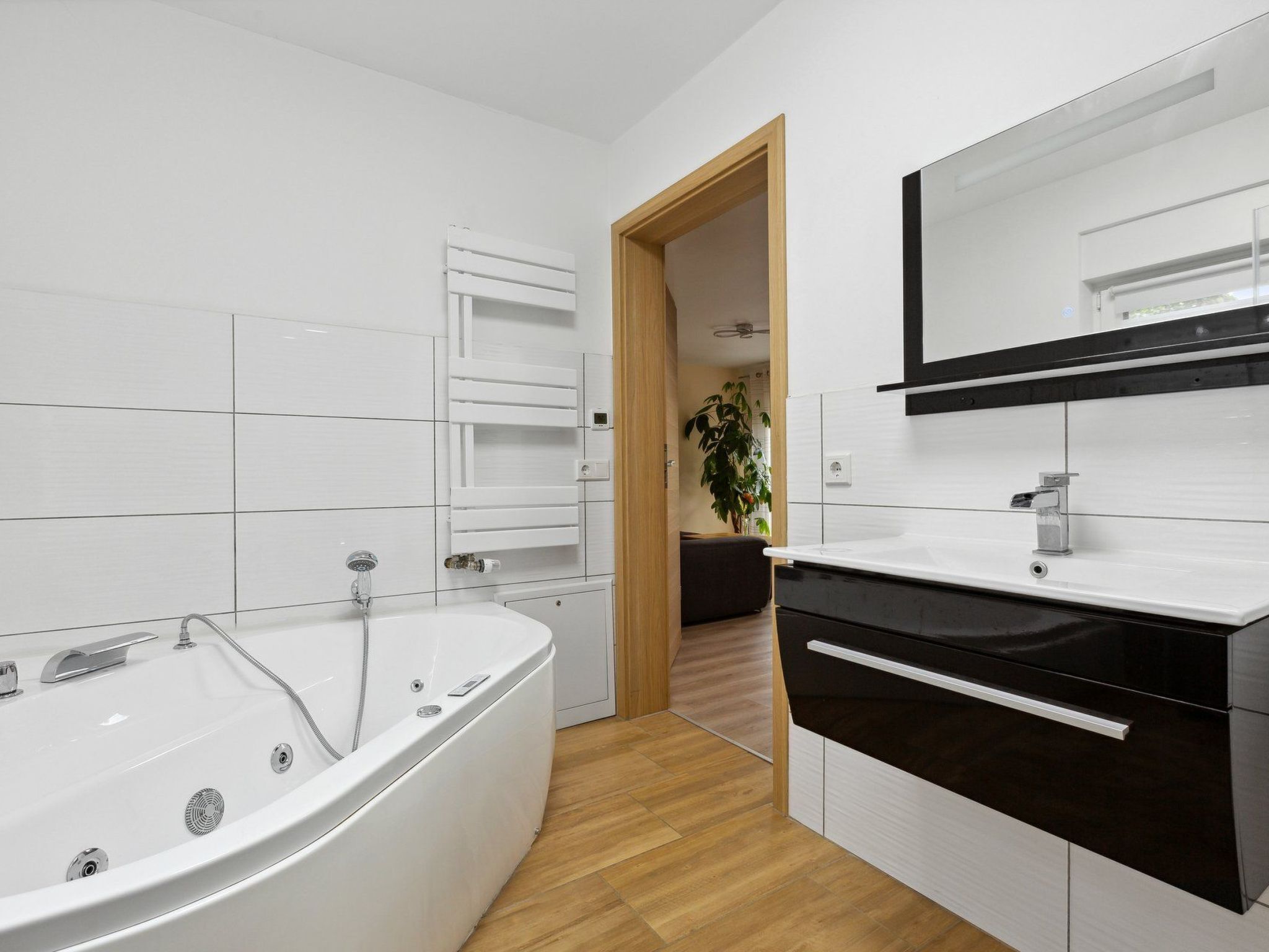 Ein modernes Badezimmer mit freistehender Badewanne, einem Schwarz-Weiß-Waschtisch und einem großen Spiegel.