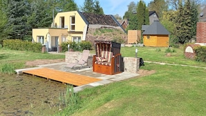 Une propriété au bord du lac, dotée d’une terrasse en bois, d’un belvédère à toit de chaume et d’une maison jaune.