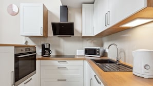 Une cuisine moderne avec des meubles blancs, un four encastré, une machine à café, un four à micro-ondes et un évier.