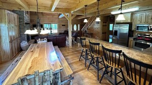 Een ruime keuken met houten balken, een lange eettafel, barstoelen en moderne apparatuur.