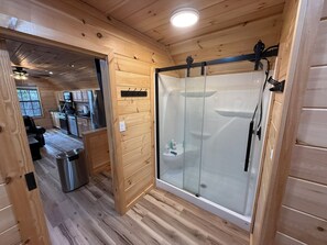 A wooden interior with a glass-enclosed shower, a kitchen area, and a seating area. - Small Cabin Over Garage w/ lake access, small dock (Sevierville)