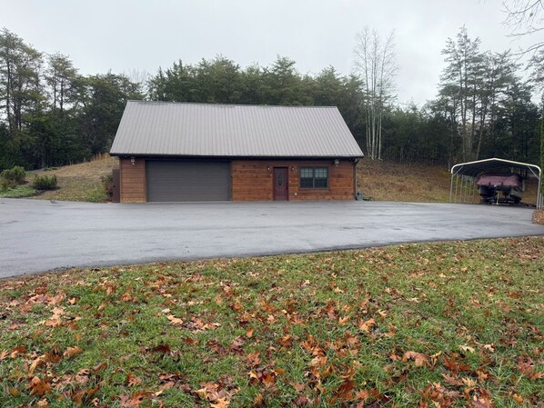 A single-story building with a large garage door, surrounded by a grassy area with scattered fallen leaves. - Small Cabin Over Garage w/ lake access, small dock (Sevierville)