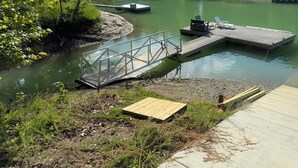 Un quai au bord de la rivière, avec un pont métallique, une plateforme en bois et une promenade en béton.