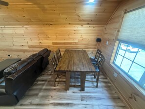A wooden interior with a dining table, chairs, a sofa, and a window with a view of a parking lot. - Small Cabin Over Garage w/ lake access, small dock (Sevierville)
