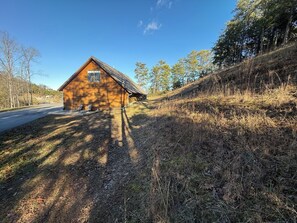 A wooden cabin with a sloped roof, situated on a hillside with a clear sky. - Small Cabin Over Garage w/ lake access, small dock (Sevierville)