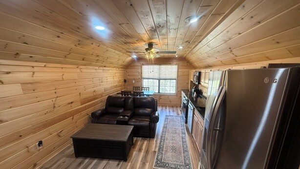 L’intérieur d’un petit chalet en bois comprend un canapé, une petite table, un réfrigérateur et une fenêtre.